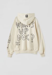 Sweat à capuche beige avec texte noir style croquis "WHAT'S UP DOC ?" dans le dos, petit texte "THAT'S ALL FOLKS" et motif pinceau sur la manche gauche.