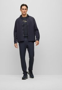 Navy button-up shirt over a black crew neck t-shirt, paired with slim-fit navy trousers and dark sneakers with yellow accents.