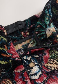 Viacfarebná kvetinová textúrovaná látka zblízka s čiernym zipsom a priehľadným gombíkom, s detailnými vzormi z nití.