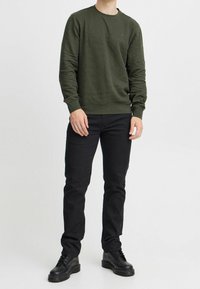 Felpa di cotone verde scuro con maniche lunghe, colletto a giro e polsini a costine; abbinata a jeans neri slim e stivali neri con lacci.