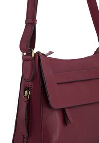 Bordeaux læderhandtaske med en glat tekstur, udstyret med en fold-over lågflap, lynlåsdetaile og hardware accenter i guld-tone.