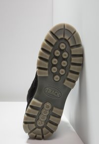 Suela de zapato negra con una superficie de goma texturizada, que presenta patrones de agarre circulares y un logotipo. Contraste claro con una suela exterior de color gris claro.