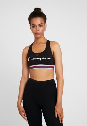 Sujetador deportivo negro con escote redondeado y logo, que presenta una banda a rayas en rojo, blanco y azul. Combinado con leggings negros de cintura alta.