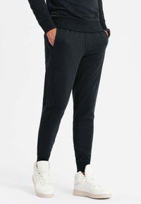 Svarta joggers med en avsmalnande passform, texturerat tyg, sidofickor och resårmidja, tillsammans med vita högskurna sneakers.