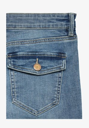 Primo piano di una tasca posteriore di jeans blu con un pattina con bottone e un passante per cintura visibile su sfondo bianco.