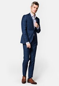 Granatowy w kratę garnitur o dopasowanym kroju, zestawiony z białą koszulą w paski i brązowymi skórzanymi butami. Szwalniczy krój, teksturowany materiał.