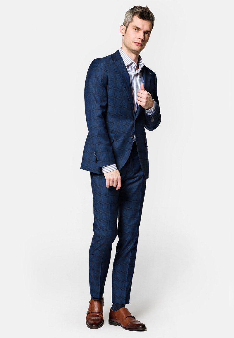Granatowy w kratę garnitur o dopasowanym kroju, zestawiony z białą koszulą w paski i brązowymi skórzanymi butami. Szwalniczy krój, teksturowany materiał.