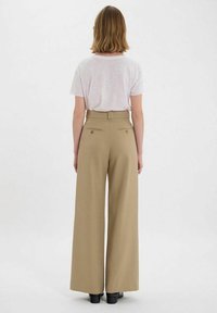 Pantalons larges beiges à taille haute, avec passants de ceinture et deux poches arrière. Associés à une chemise à manches courtes rose clair.
