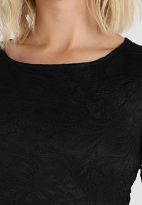 Black lace top with a smooth texture, featuring a floral pattern and a scoop neckline. The fabric appears lightweight and sheer.