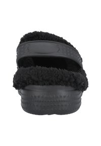 Chausson noir avec un dessus en texture pelucheuse, une semelle en caoutchouc et un motif à points pour une bonne adhérence. Design ouvert avec une seule lanière.