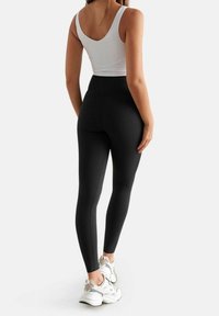 Leggings neri a vita alta realizzati in tessuto elasticizzato, con una texture liscia. Indossati con un top bianco e scarpe da ginnastica bianche.