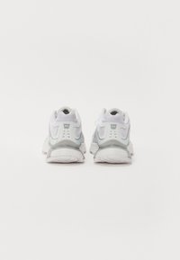 Bílé a světle šedé sportovní boty s prodyšným síťovaným svrškem, polstrovanou podrážkou a reflexním logem na patě.