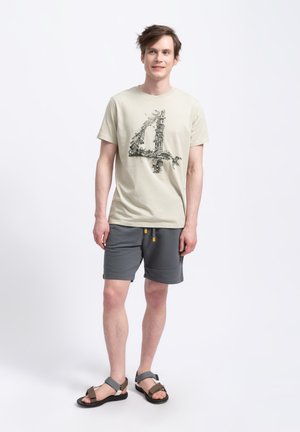 Beige katoenen T-shirt met een grafische print van het cijfer 4, gecombineerd met grijze shorts en bruine sandalen met verstelbare bandjes.