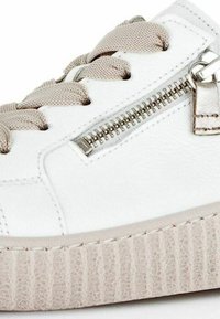 Baskets en cuir blanc avec une semelle beige striée, des accents texturés, des lacets en tissu et un détail en métal avec fermeture éclair sur le côté.