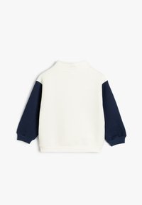 Sweat-shirt à encolure ronde avec un corps blanc et des manches bleu marine. Il dispose d'un col montant et de poignets côtelés. Tissu doux, design décontracté.