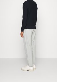 Granatowy sweter z prążkowanym wykończeniem, jasnoszare spodnie o luźnym kroju oraz kremowe buty na masywnej podeszwie, widziane od tyłu.