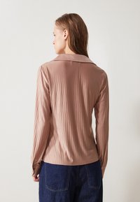 Long-sleeve, ribbed blouse in a soft beige color with a flat collar, smooth texture, and buttoned cuffs, paired with dark denim.