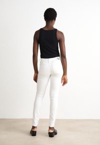 Top negro de tirantes, jeans skinny blancos con bolsillos traseros y mules de tacón negro. Tejido suave y silueta ajustada con el logo de CK en la cinturilla.
