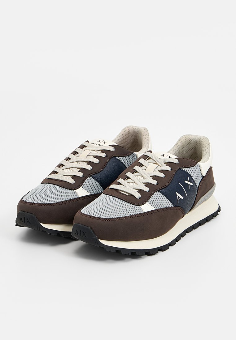 Zapatillas gris y marrón con materiales de malla y ante. Presentan una franja lateral azul marino y cordones beige en contraste. Suela de goma texturizada.
