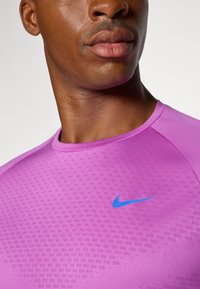 Purple athletic shirt with textured fabric, round neckline, and blue Nike swoosh logo on the left chest.
