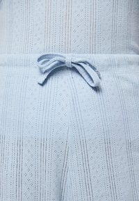 Gaiši zila adīta auduma ar strukturētām svītrām un mazām dimanta rakstām. Aprīkota ar auklu jostā.