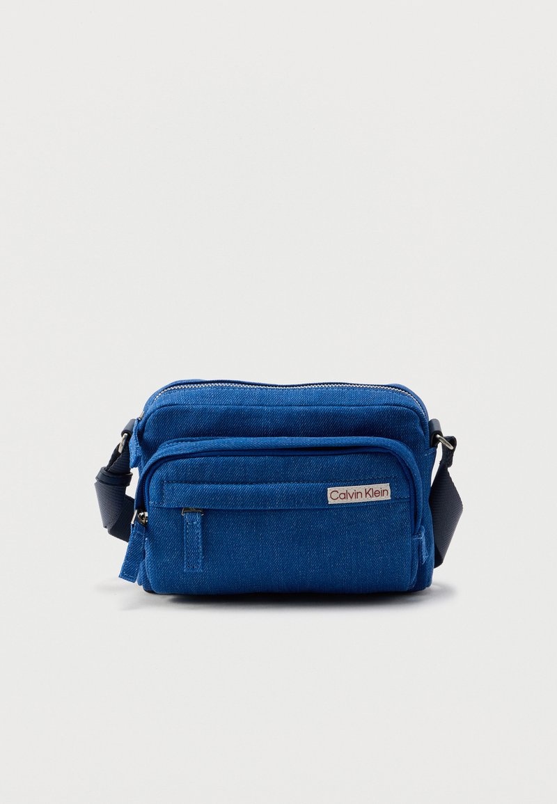 Μπλε υφασμάτινη τσάντα crossbody με υφασμένη επιφάνεια, που διαθέτει πολλαπλές τσέπες με φερμουάρ και ιμάντα ώμου. Λογότυπο Calvin Klein στο μπροστινό μέρος.