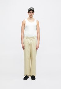 Lett, ribbet hvit tanktopp, beige vide bukser, svarte sneakers og en grå caps. Enkelt design uten synlige mønstre eller detaljer.