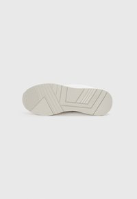 Die Sohle des weißen Sneakers besteht aus einem strukturierten Gummi-Material mit unterschiedlichen Mustern, darunter horizontale Rillen und ein dezentes Logo-Detail.