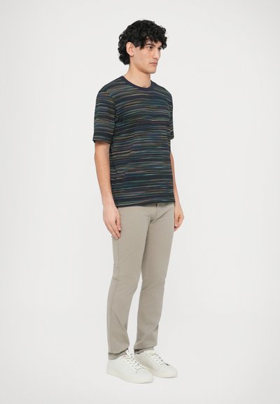 Többszínű csíkos rövid ujjú póló, világos bézs nadrággal és fehér tornacipővel párosítva. A póló kerek nyakkivágással és bő szabással rendelkezik.