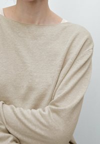 Beżowy sweter dzianinowy z szerokim dekoltem i długimi rękawami. Tkanina wydaje się miękka z delikatną fakturą, ma luźny krój i minimalny design.