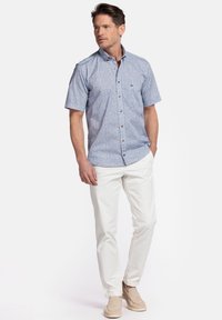 Chemise à manches courtes, à boutons, de couleur bleu clair avec un petit motif floral ; associée à un pantalon blanc et des chaussures beiges.