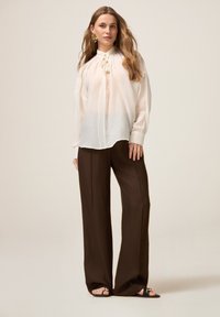 Lichte, doorschijnende blouse met een gathered halslijn, gecombineerd met brede, bruine broek. Het ensemble heeft een eenvoudige, natuurlijke kleurenpalet en een gladde textuur.