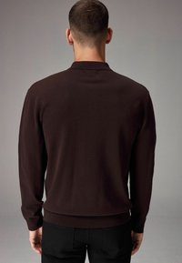 Dunkelbrauner langärmelliger Strickpullover mit einem gerippten Kragen und Saum, der eine glatte Textur und eine figurbetonte Silhouette aufweist.