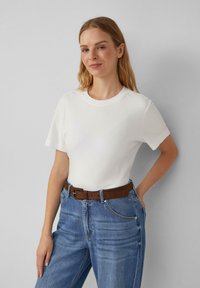 T-shirt blanc à manches courtes avec un col rond, associé à un jean en denim bleu taille haute et une ceinture en cuir marron.