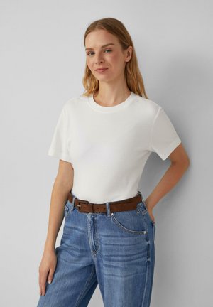 Weißes Kurzarm-T-Shirt mit rundem Halsausschnitt, kombiniert mit blauen High-Waist-Jeans aus Denim und einem braunen Ledergürtel.