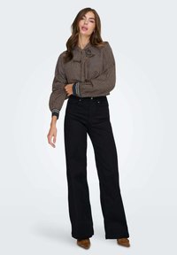Blusa marrone con motivo e fiocco al colletto, maniche lunghe con polsini a contrasto, abbinata a pantaloni neri a vita alta e a gamba larga.