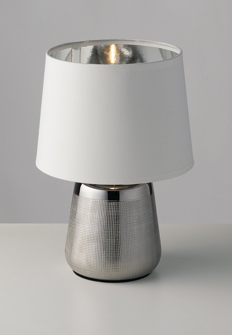 Lampa stołowa z metalową podstawą o srebrzystej fakturze i białym abażurem z tkaniny. Wewnętrzny abażur ma metaliczne wykończenie, odbijające światło.