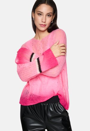 Rosa gestrickter Pullover mit einem Farbverlauf von hell- zu dunkelrosa, mit gerippten Bündchen in Schwarz und Weiß. Getragen mit schwarzen Leggings.