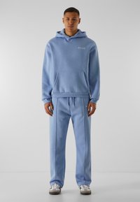 Lyseblå hoodie og sæt af sweatpants lavet af bomuldsblanding. Har en frontlomme, elastisk talje og diskret logodetalje på brystet.
