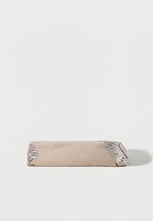 Tessuto beige piegato con ricamo floreale dettagliato bianco e nero su uno sfondo bianco semplice.