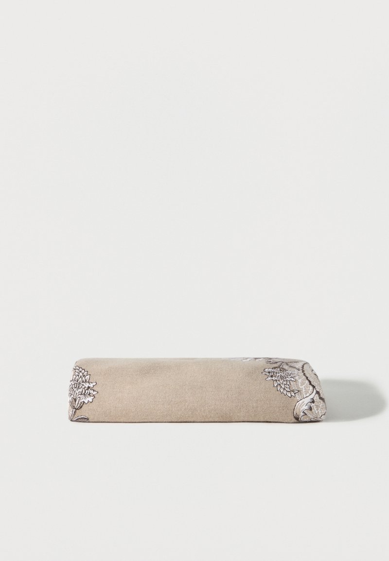 Tissu beige plié avec une broderie florale blanche et noire complexe sur un fond blanc uni.