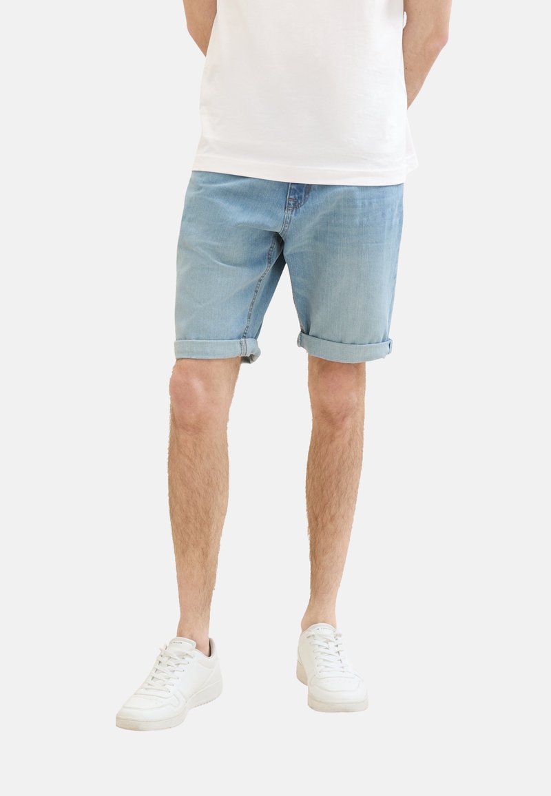 Vaaleansiniset denim-shortsit, joissa on käännetyt lahkeet, yhdistettyinä valkoisiin lenkkareihin. Materiaali on sileä, rento malli ilman näkyviä kuvioita tai yksityiskohtia.