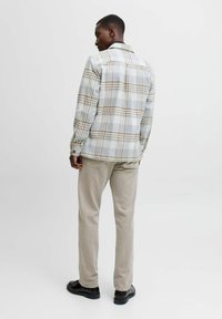 Camisa de cuadro gris y beige con cuello clásico, puños abotonados y corte recto, combinada con pantalones beige claros y zapatos negros.