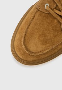 Tan suede shoe with a rounded toe, thin lacing, and rubber sole. Features a smooth texture and neatly stitched detailing.