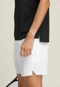 Pantalones cortos deportivos blancos con una ligera abertura lateral, fabricados en material ligero. Presentan un pequeño logo en relieve en la parte inferior izquierda.