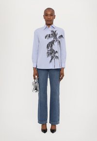 Blau-weiß gestreiftes Langarmhemd mit einem Palmbaum-Print, kombiniert mit ausgestellten blauen Jeans und schwarzen spitzen Absatzschuhen. Silberne Handtasche.