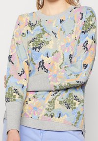 Flerfärgad huvtröja i mjukt material, med ett blommigt och abstrakt mönster i pastelltoner och grå ribbade muddar.