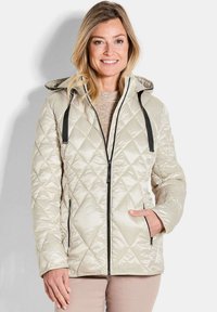 Gepolsterte, hellbraune Daunenjacke mit Kapuze, versehen mit schwarzen Akzenten, Reißverschlusstaschen und einer figurschmeichelnden Passform. Zarte, glanzende Textur.