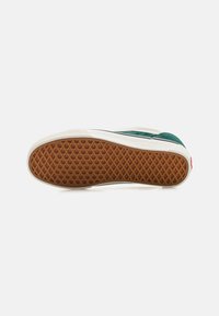 El zapato cuenta con una suela de goma con un patrón de diamante, parte superior de ante verde, mediode suela blanca y una franja de acento negra.