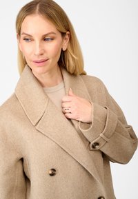Beige uldblandet dobbeltradet frakke med en stor klippet krave, tre brune knapper og opfoldede manchetter, der har en blød texture og en skræddersyet pasform.
